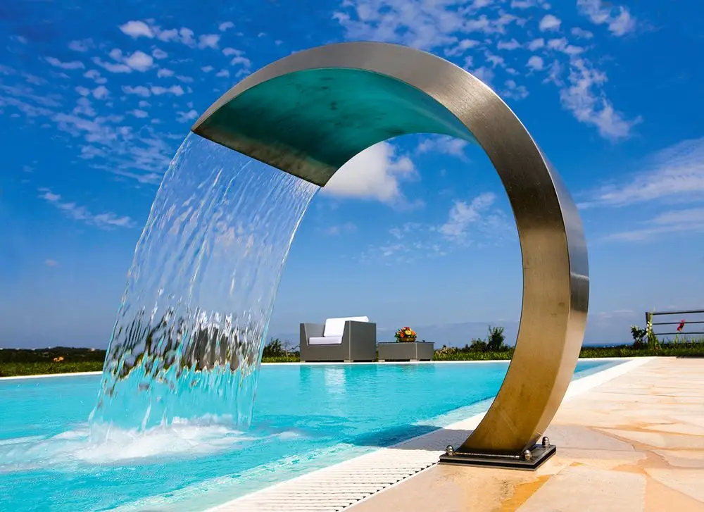 Wasserfall aus Edelstahl, der in ein Poolbecken fließt. Im Hintergrund eine moderne Sitzgelegenheit. Produkt von Grünbeck zur Verwendung in Poolanlagen.